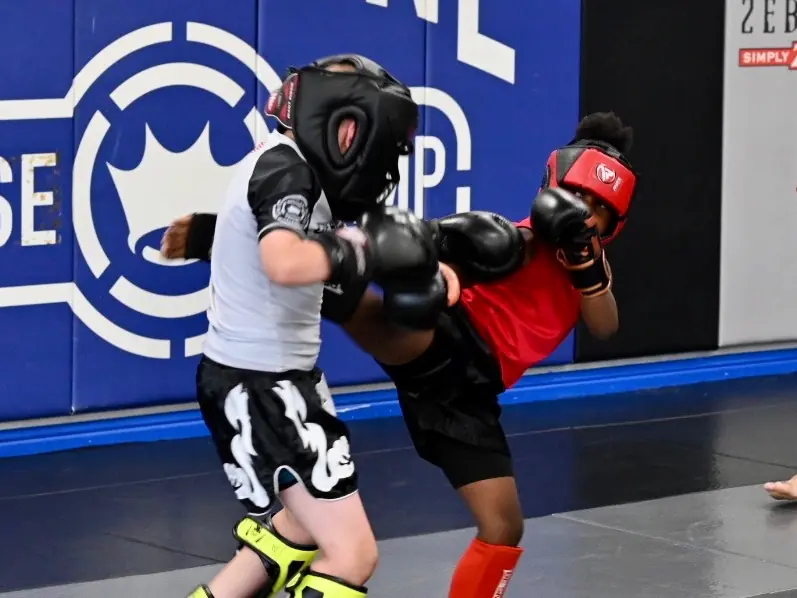 Two young kickboxers in headgear spar in front of the Dethrone Base Camp wall.